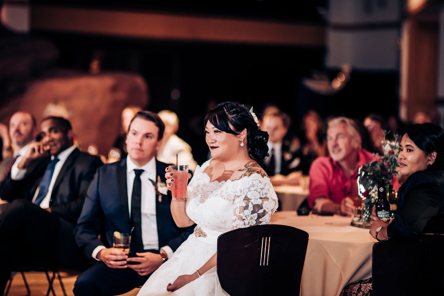 A wedding reception scene shows guests seated at tables while someone raises a glass in celebration.