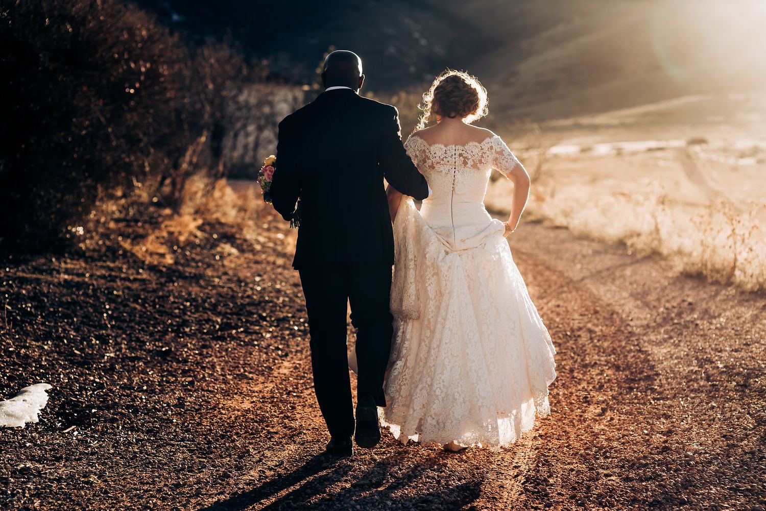 Wedding couple walking together at sunset with mountains in background.