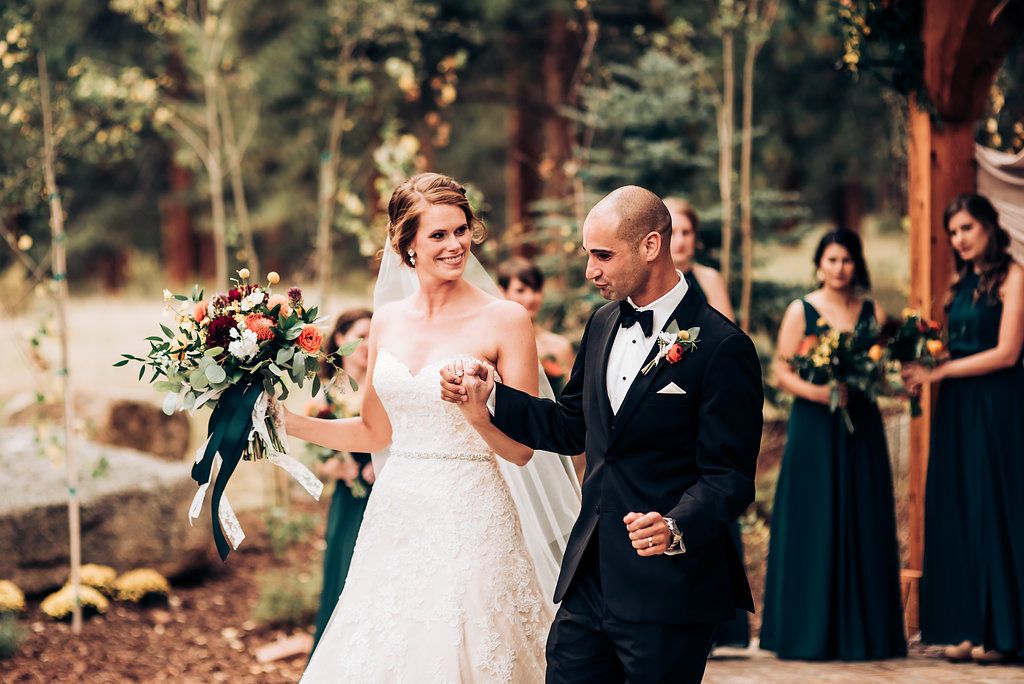 Joyful wedding celebration under wooden pergola with bridesmaids in navy dresses in background.