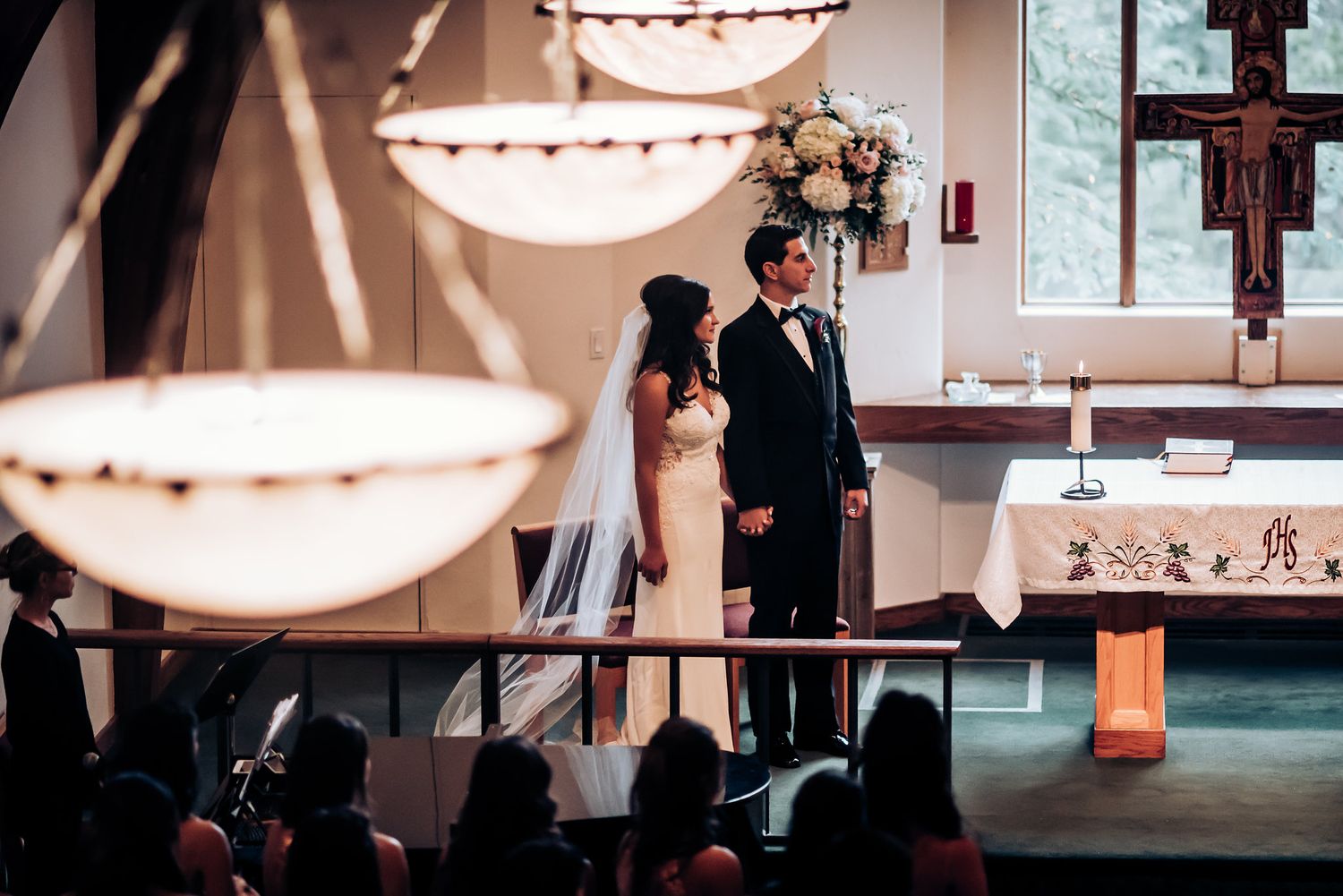 Wedding ceremony under elegant bowl chandeliers in a modern church sanctuary.