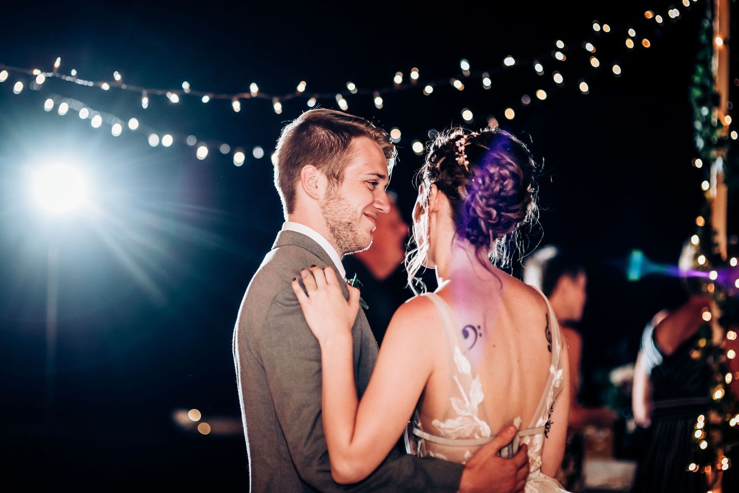Couple shares romantic dance under twinkling lights at evening wedding reception.