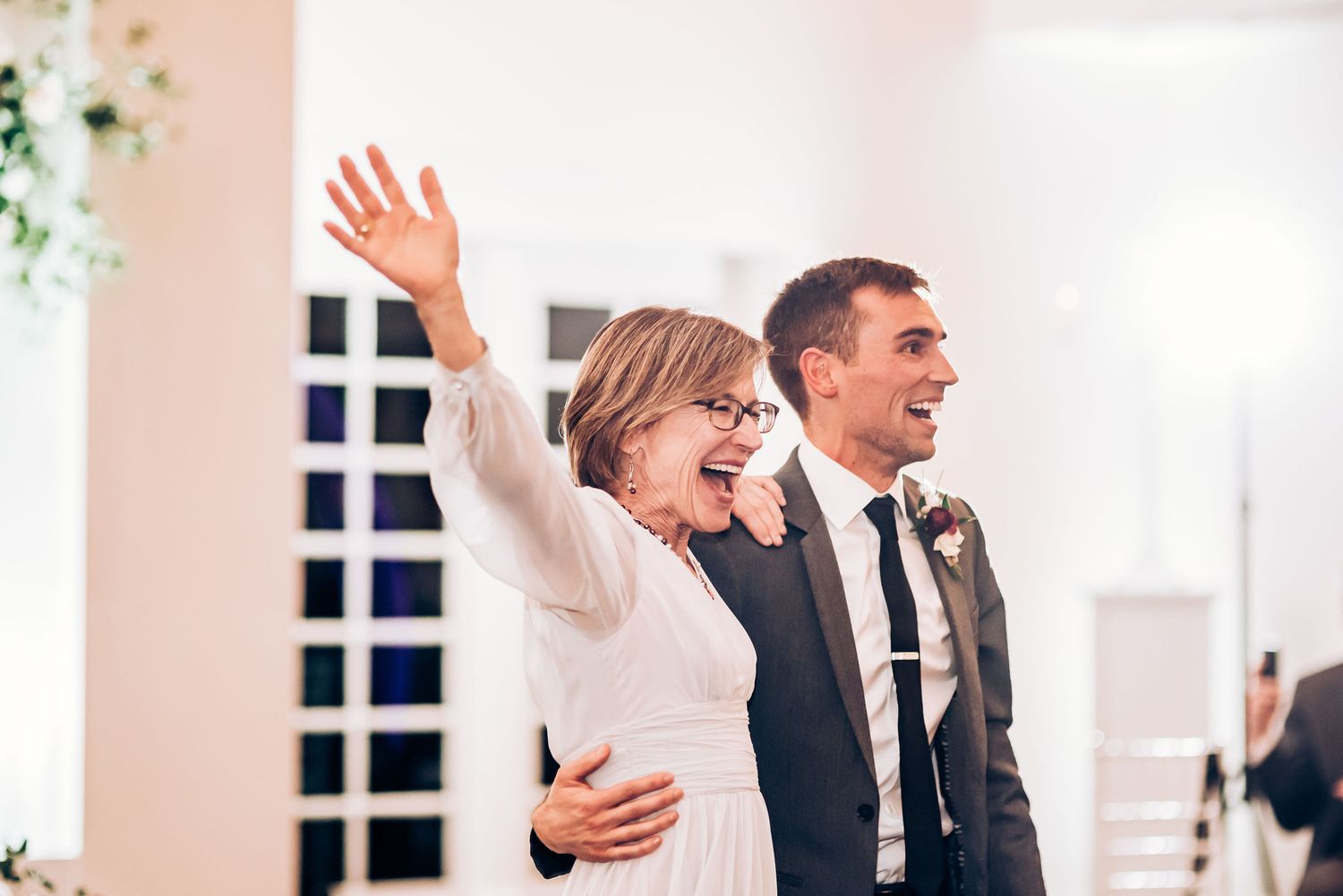 Happy couple raises their arms joyfully during a wedding celebration in an elegant white venue.