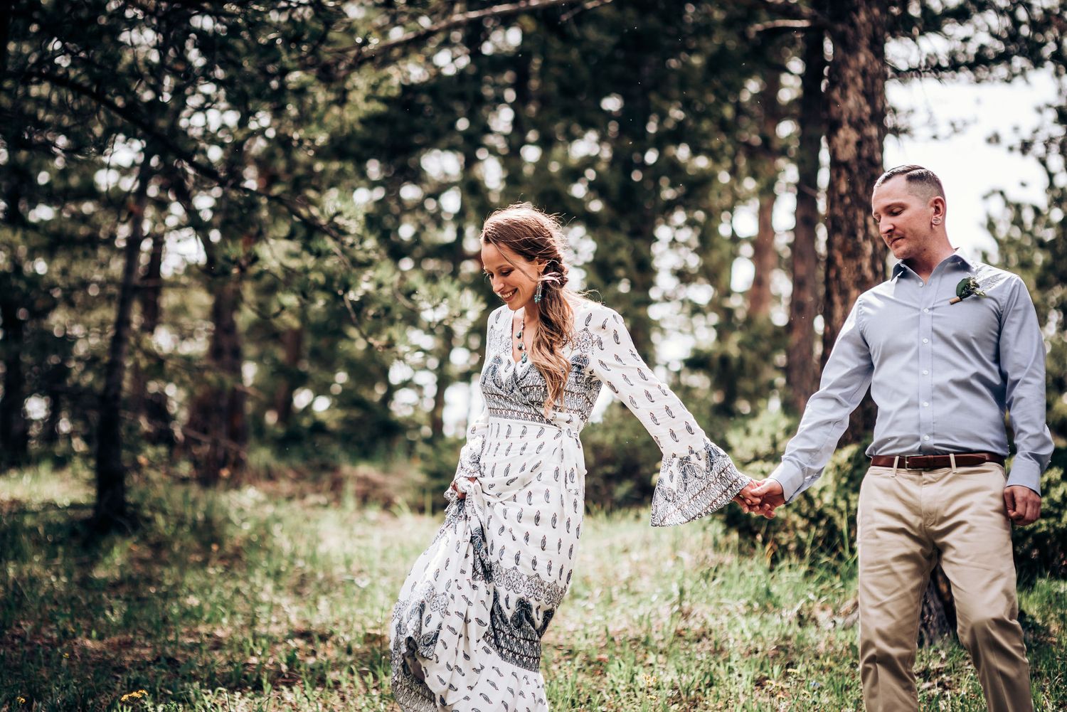 A couple shares a playful moment while walking through a sunlit forest.