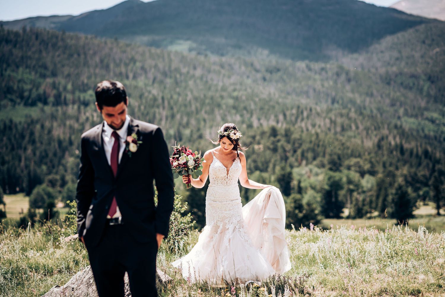 Couple walks through mountain meadow during their wedding photoshoot with dramatic landscape.
