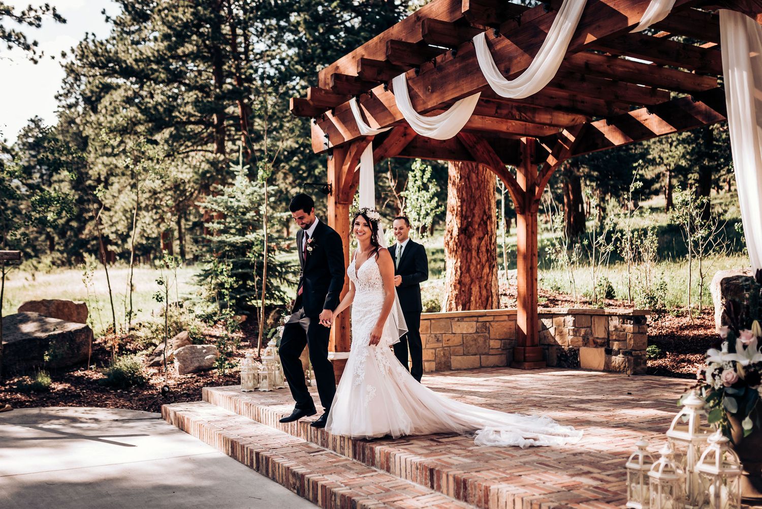 Wedding ceremony at rustic wooden pavilion with brick steps and mountain backdrop.