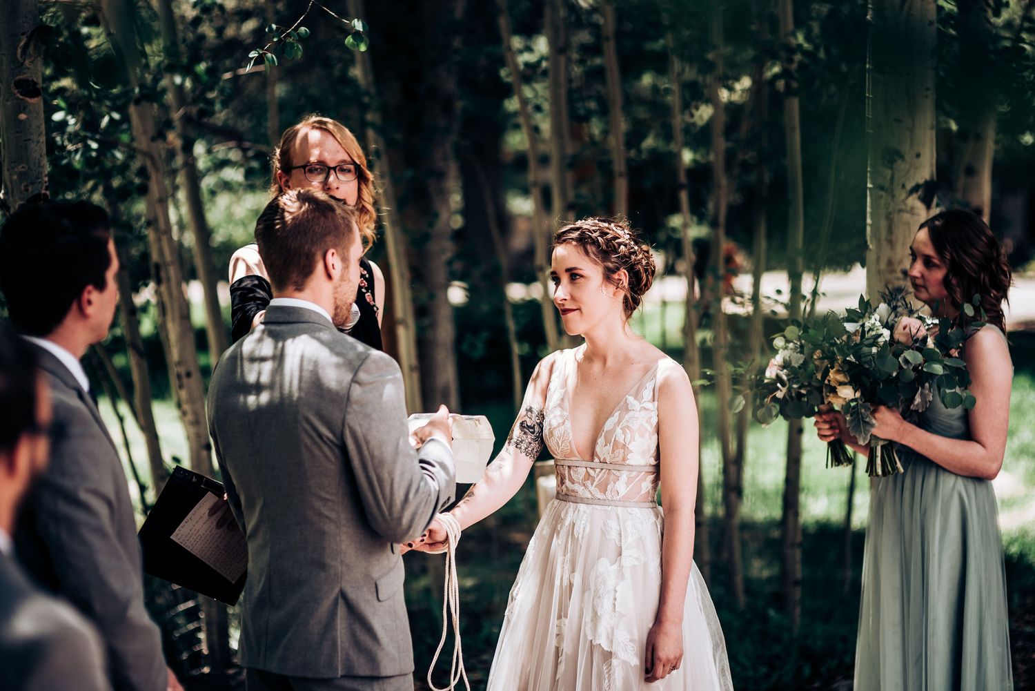 An emotional wedding ceremony moment captured in a forest setting with bridesmaids looking on.