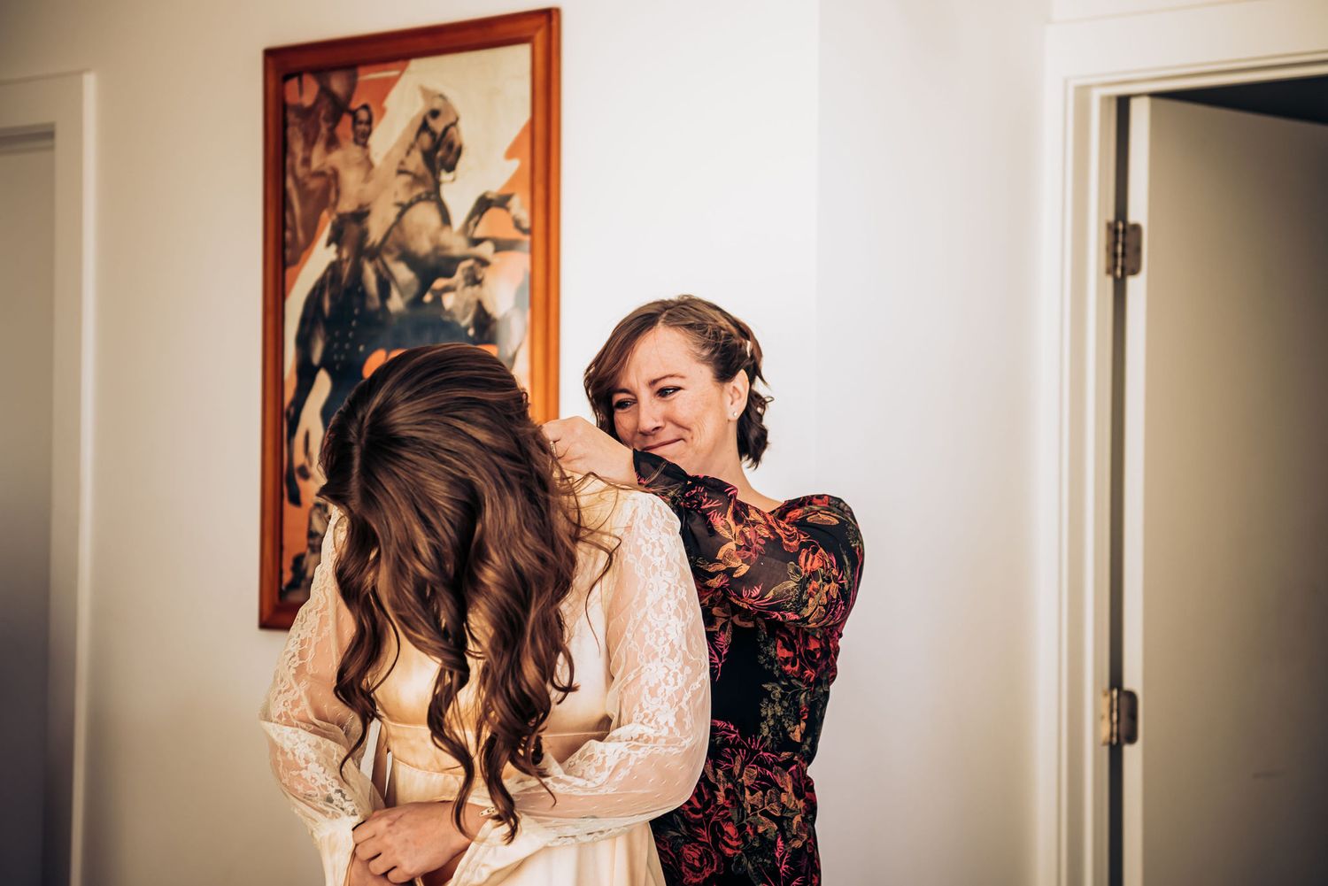 Two people share an intimate moment during wedding preparations with one helping adjust the other's outfit.