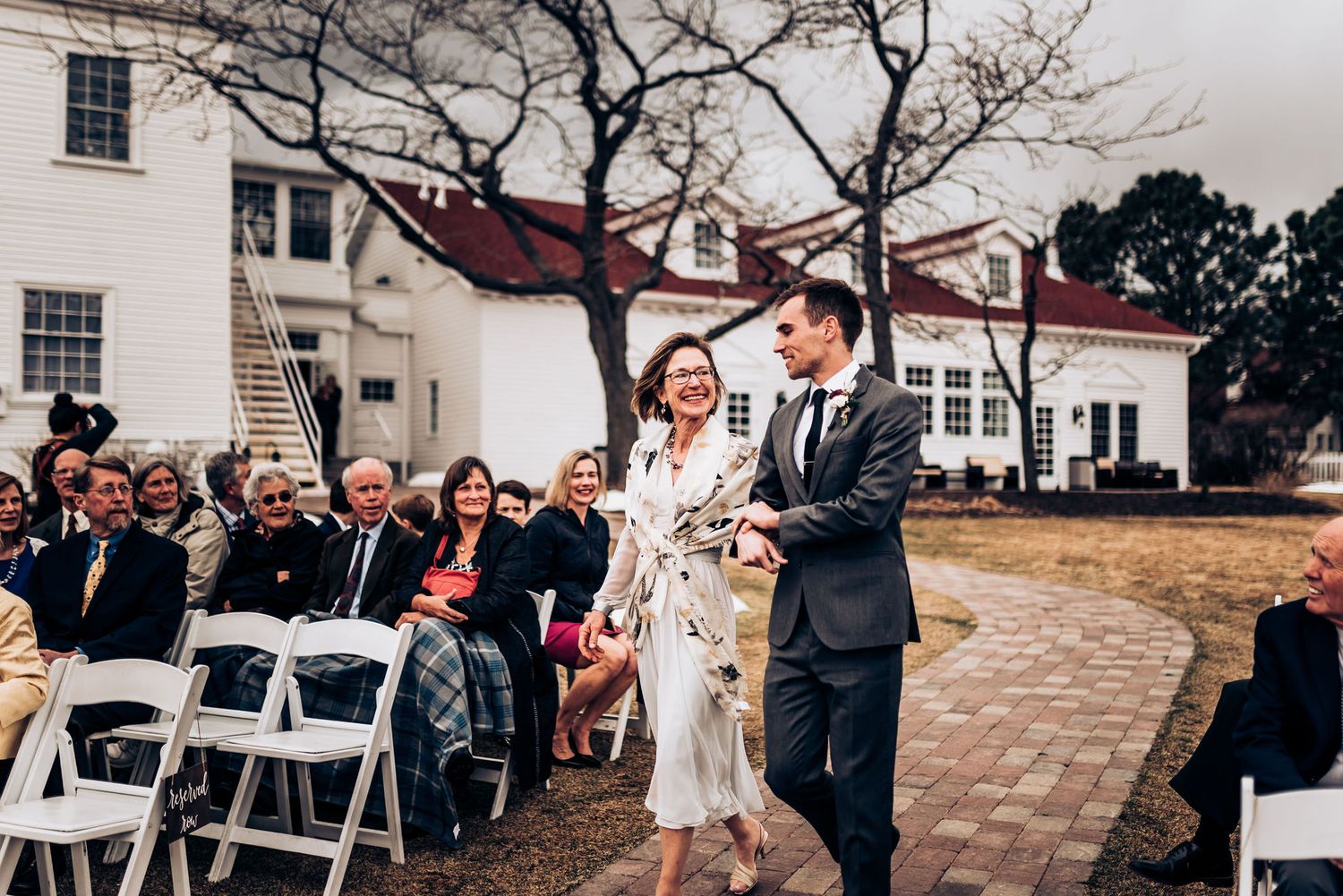 Wedding ceremony exit along brick pathway with guests seated on white chairs.