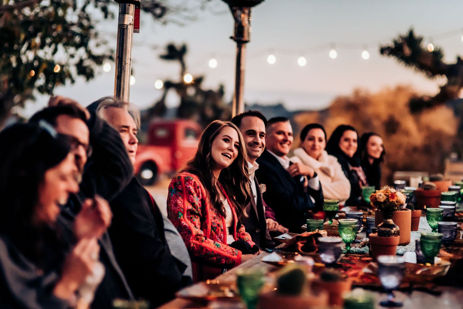 Long dining table set up outdoors with string lights and desert landscape backdrop.