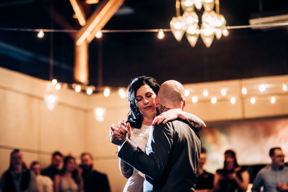 Couple sharing first dance under string lights in an intimate wedding reception venue.