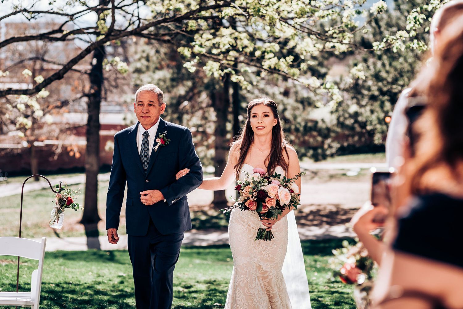 Spring wedding processional with blooming trees and guests looking on during ceremony.