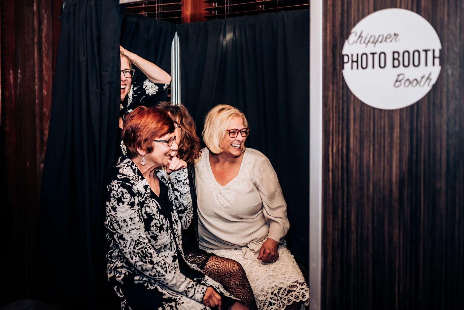 Two people sharing a laugh in front of a vintage photo booth sign.