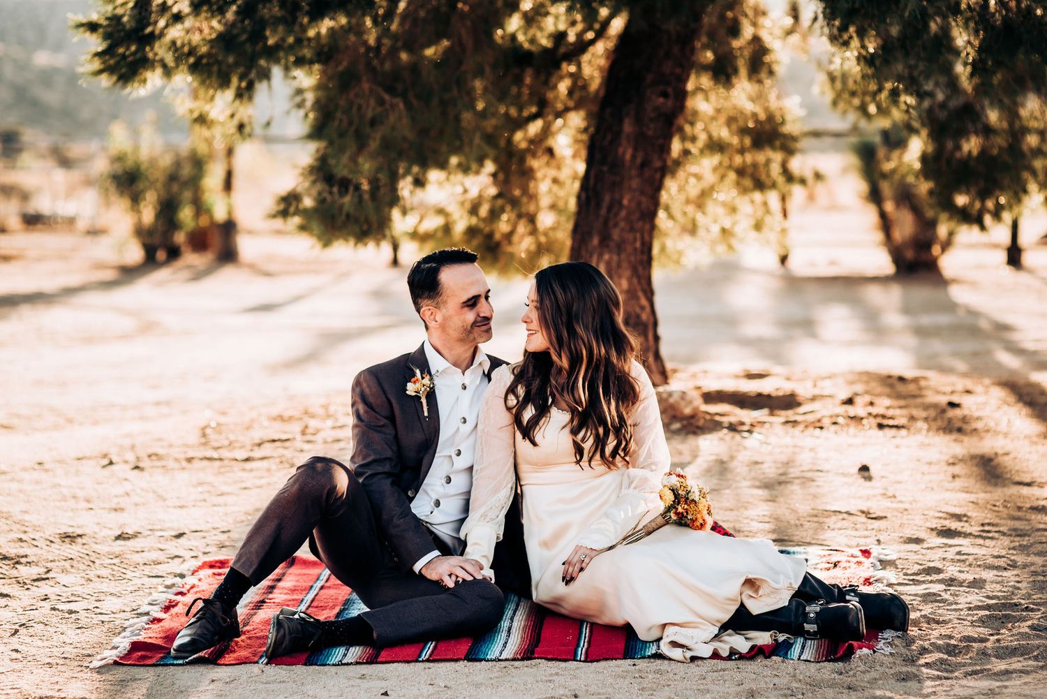 A romantic couple sharing an intimate moment on a striped blanket beneath a shady tree.