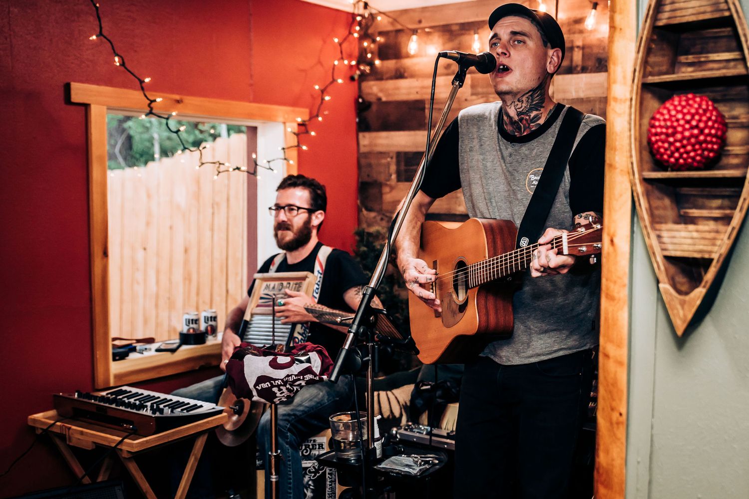 Musicians performing with guitars and equipment in a rustic room with string lights.