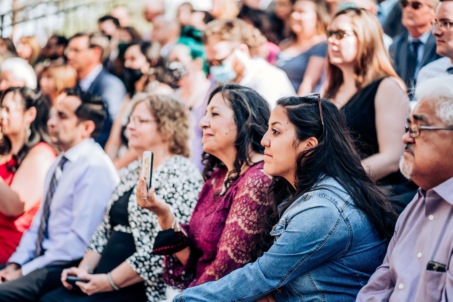 Wedding guests smiling and enjoying ceremony from audience seats outdoors.
