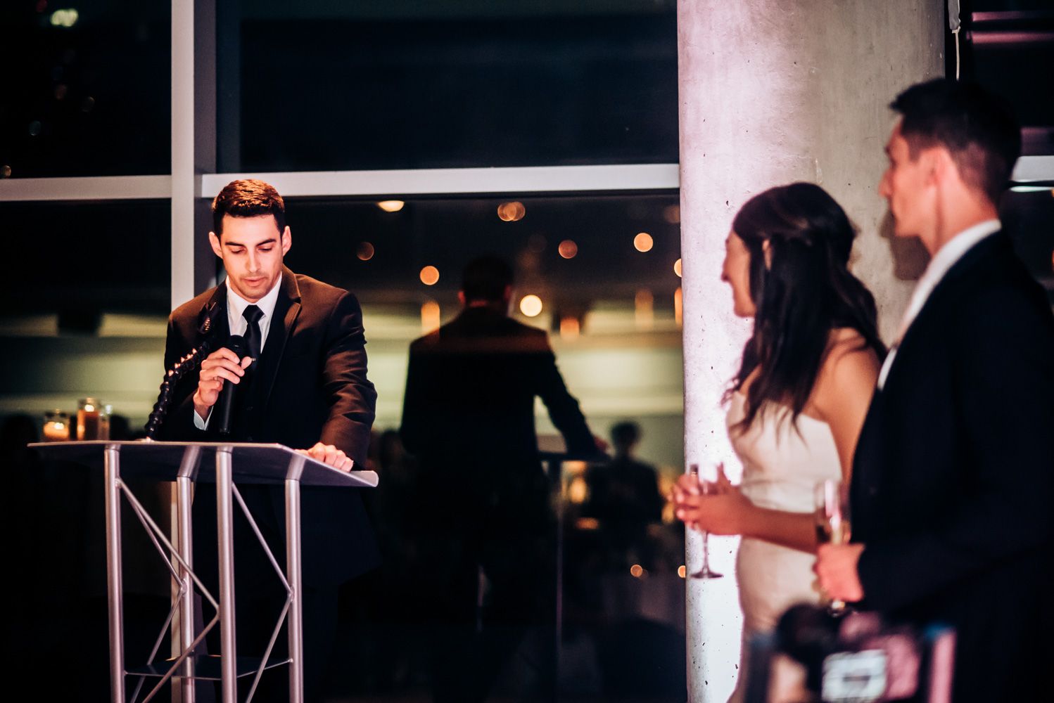 Wedding reception speech being delivered from podium during evening celebration.