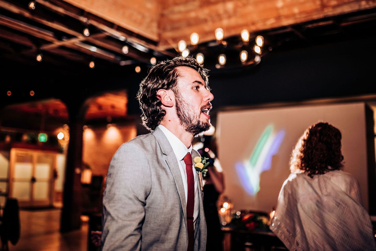 Person in formal attire singing or speaking passionately at an indoor event with mood lighting.