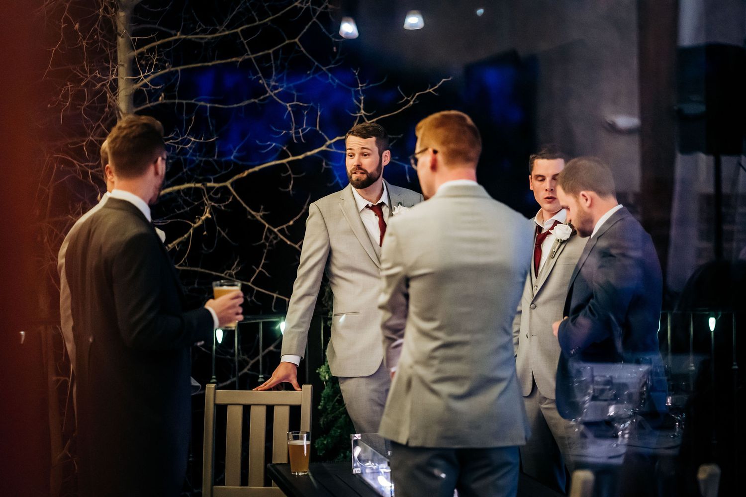 A group of groomsmen in grey suits having a casual conversation during the reception.