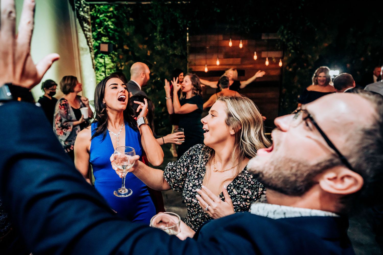 Party guests enjoying drinks and laughter at a festive celebration with ambient lighting.