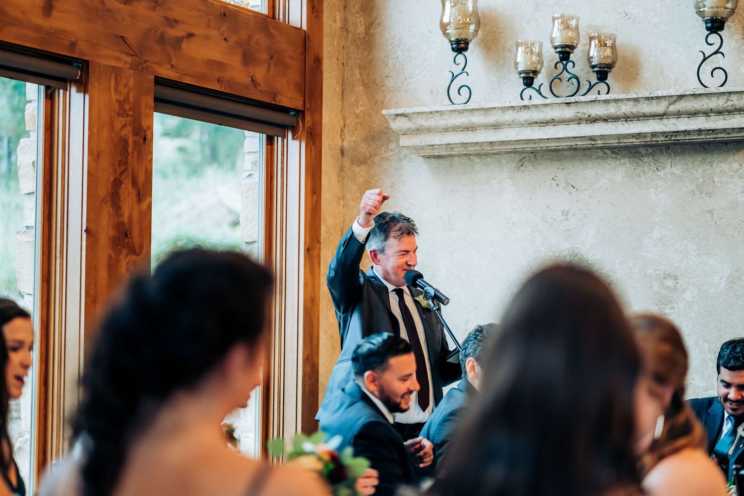 Guests celebrate joyfully during an indoor wedding reception with rustic wood beams and elegant lighting.