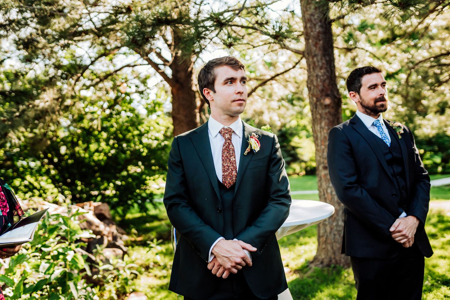 Two people in formal attire stand solemnly during an outdoor ceremony.