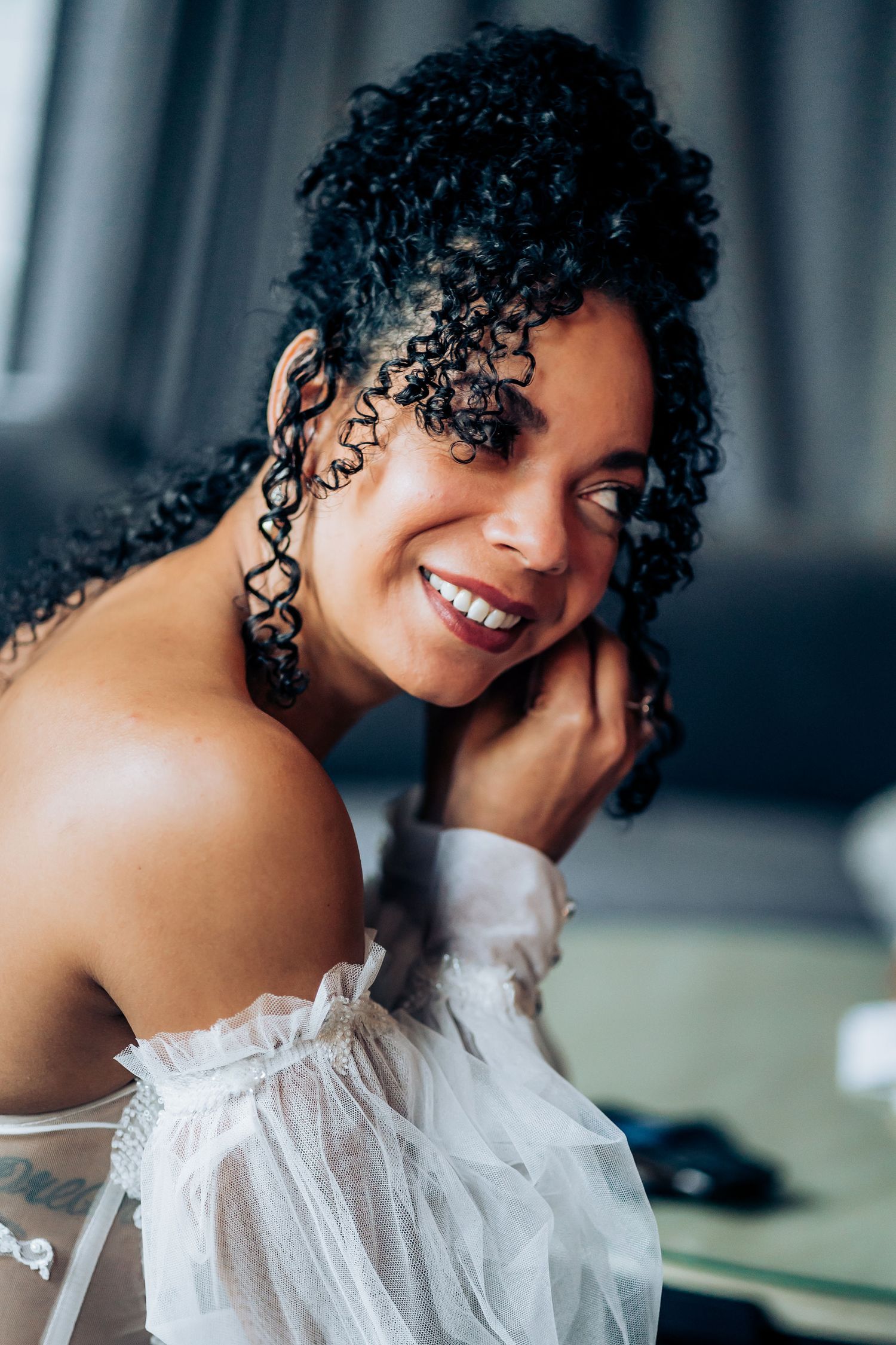 A bridal portrait showing off natural curls and an off-shoulder white tulle gown.