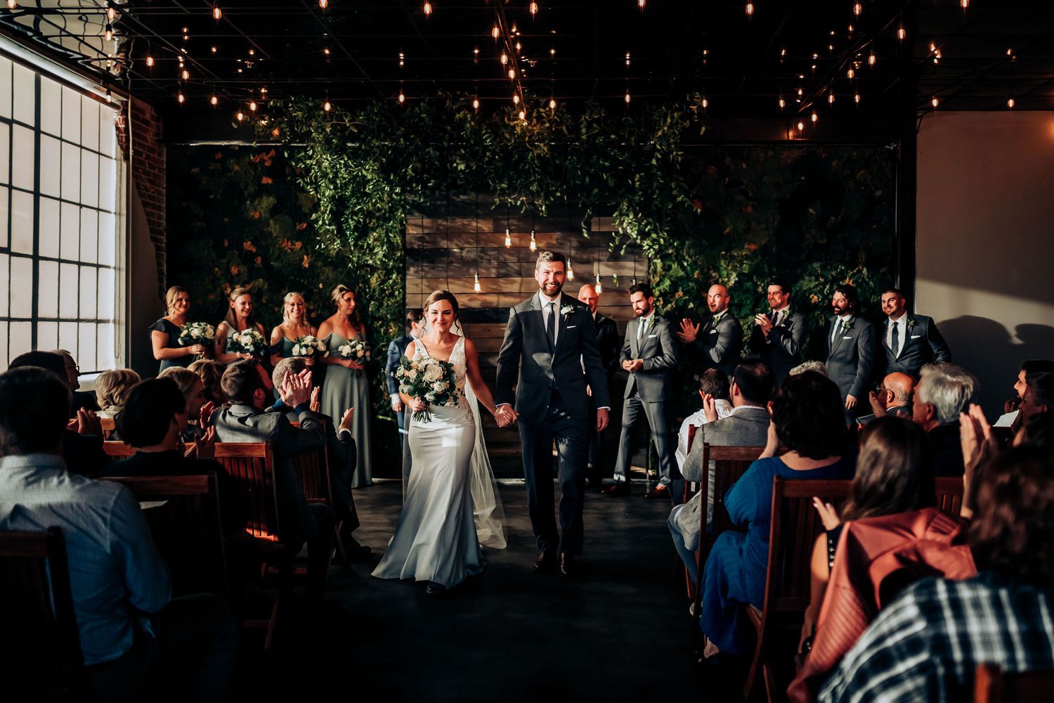 Wedding ceremony in modern industrial space with hanging lights and exposed brick.