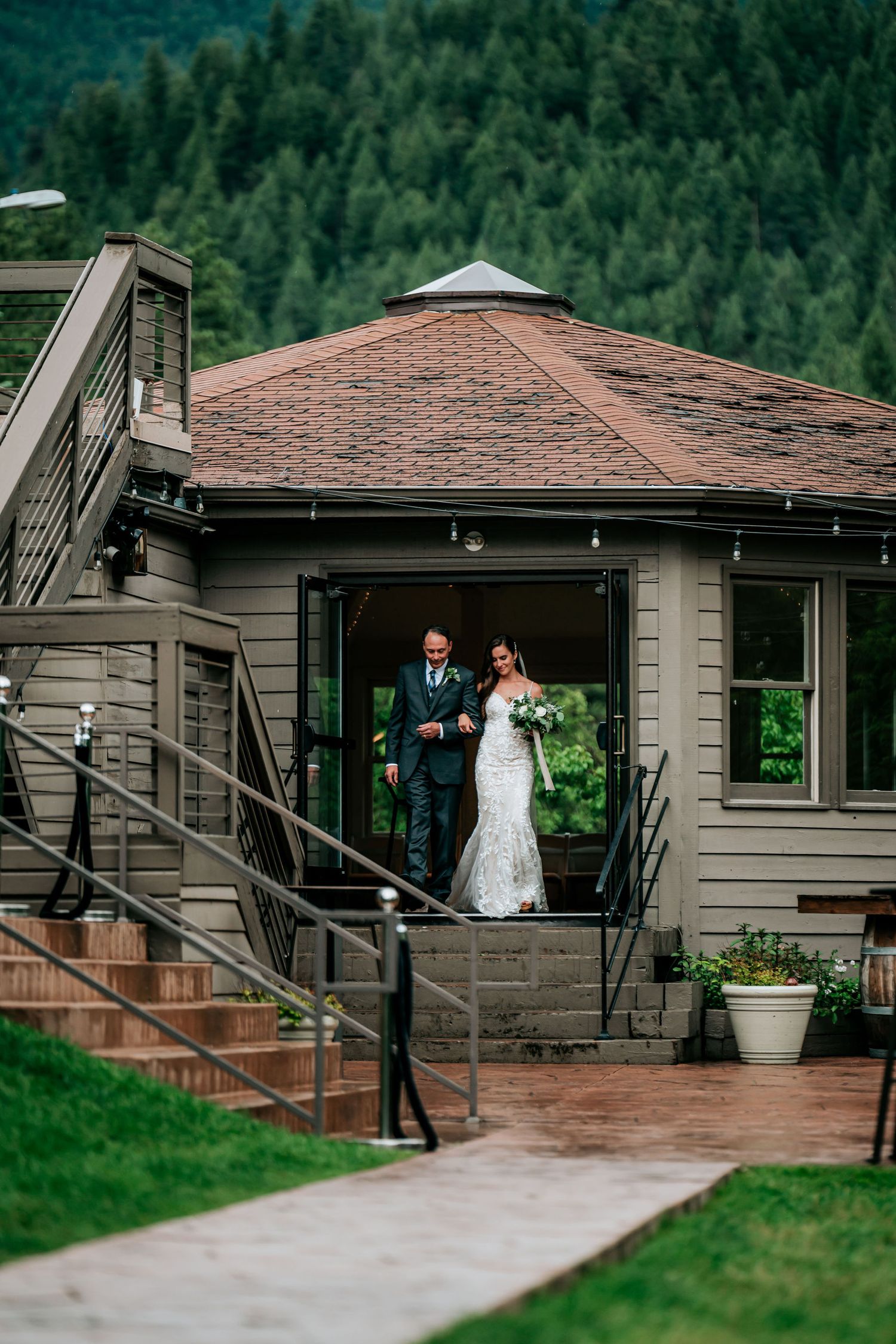 Newlyweds exit a modern mountain lodge with forest views in the background.
