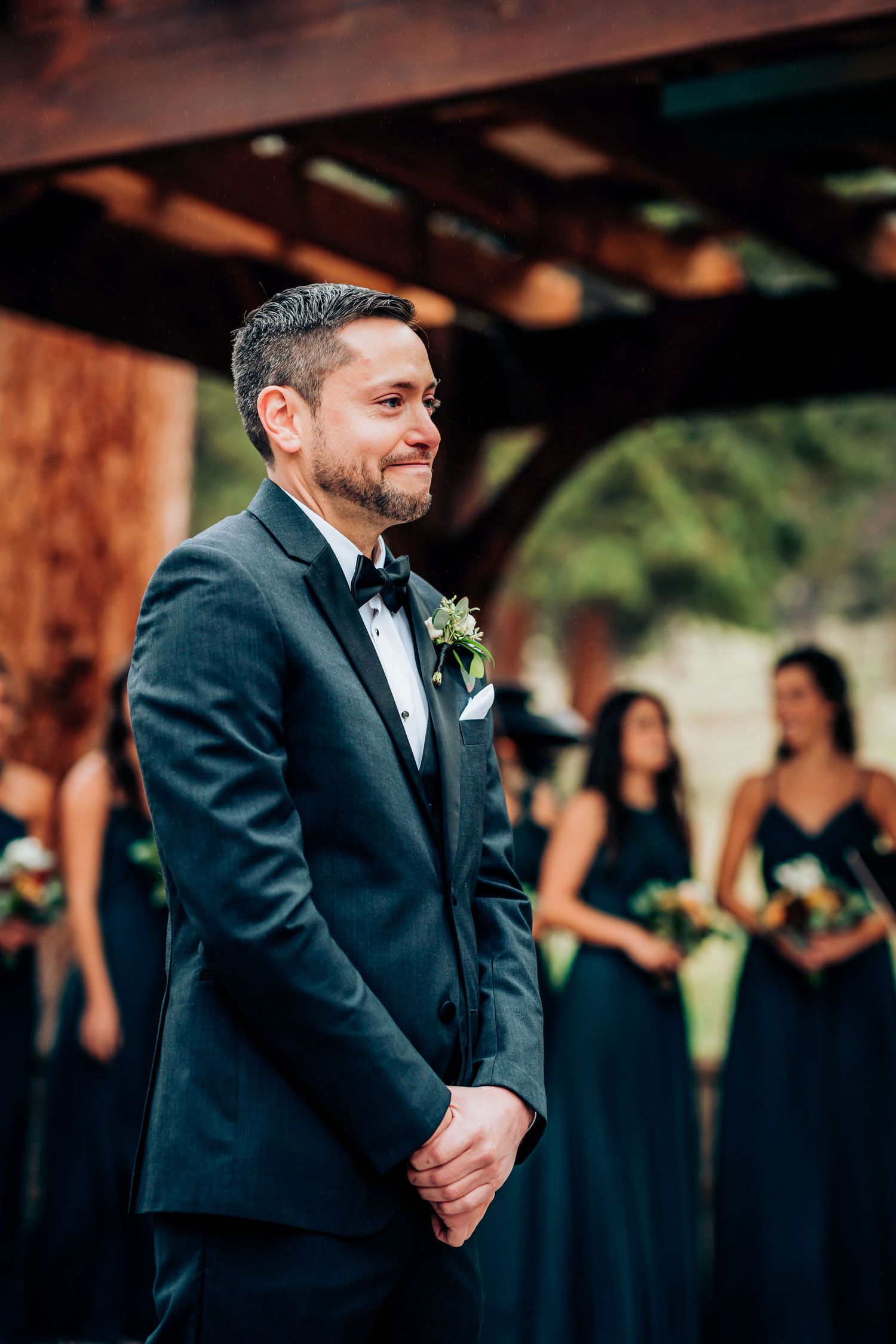 An elegant outdoor wedding ceremony with attendants in formal attire under a wooden pavilion.