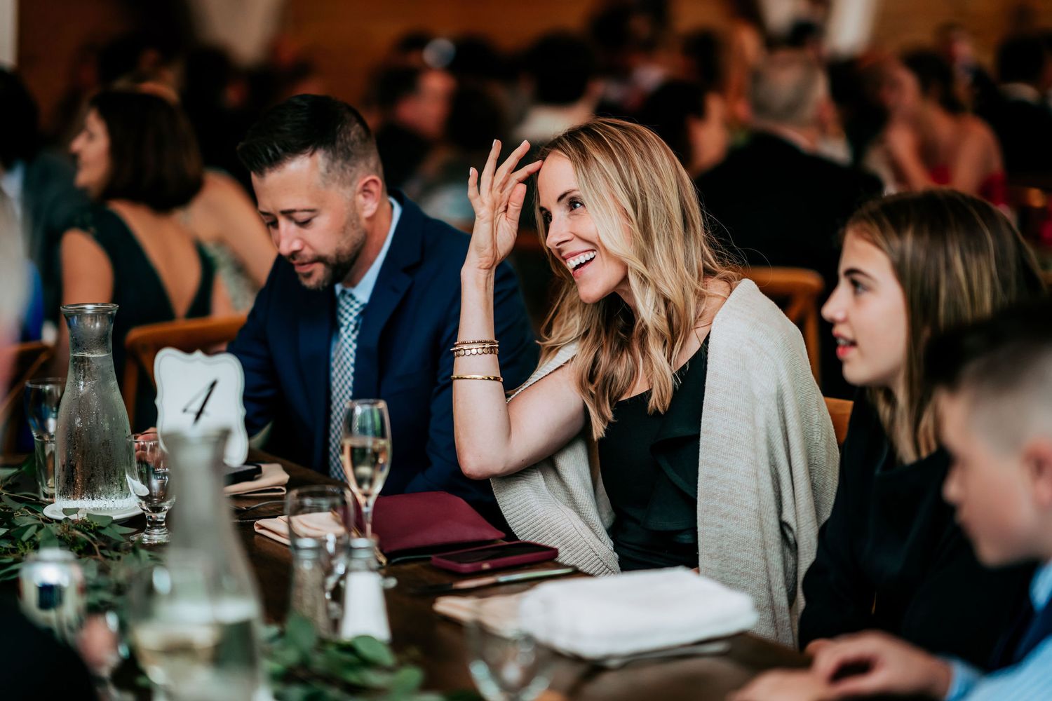 Wedding guests enjoying dinner and conversation at an elegant reception banquet table with wine glasses.