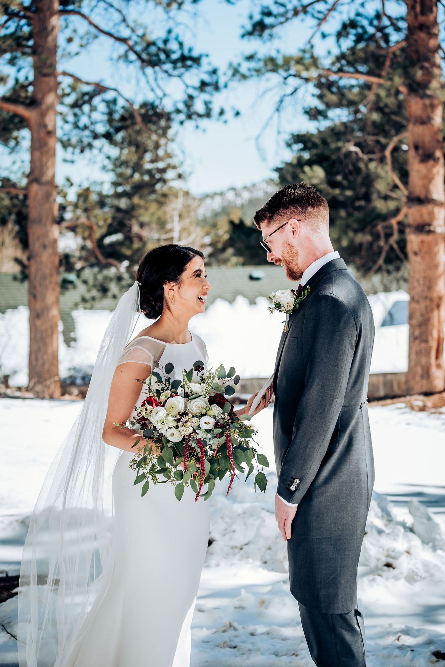 A candid wedding photo showing laughter between newlyweds in a winter mountain setting.