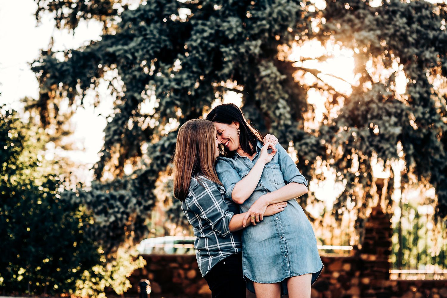 A loving couple embracing outdoors at sunset with golden light filtering through evergreen trees.