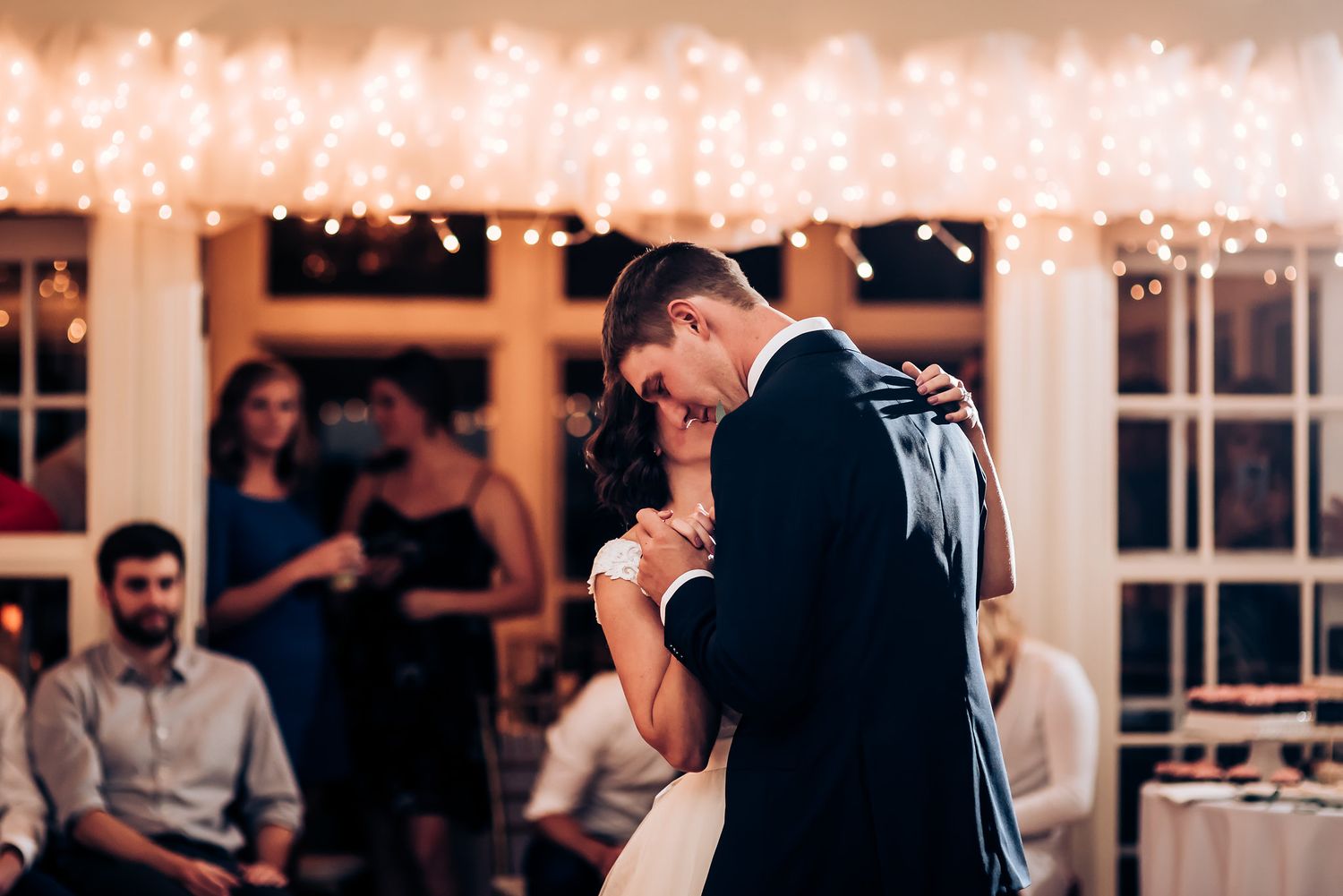 Intimate dance moment captured at evening wedding reception with string lights and guests watching.