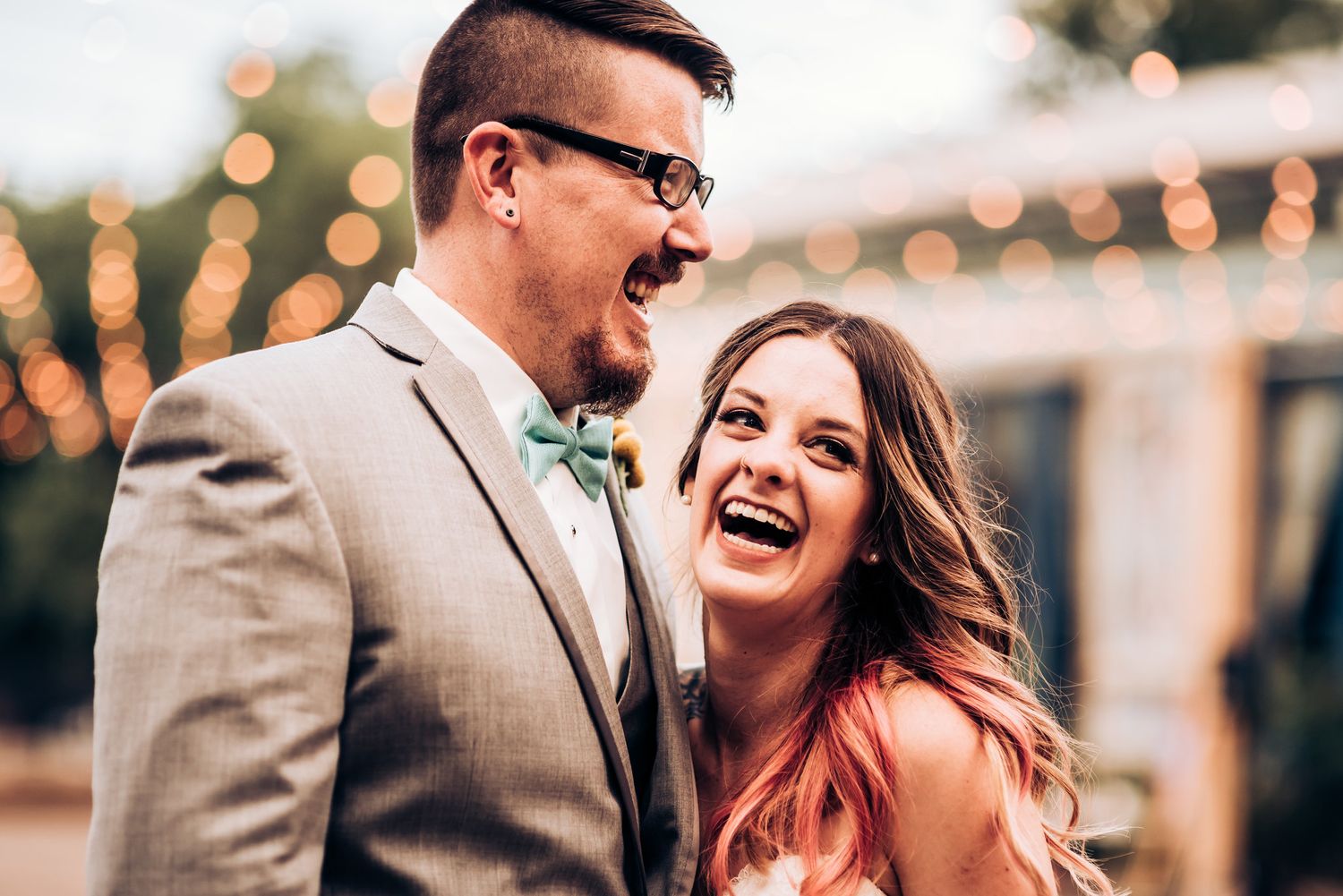 A joyful moment between a couple laughing together at an outdoor wedding celebration with string lights.