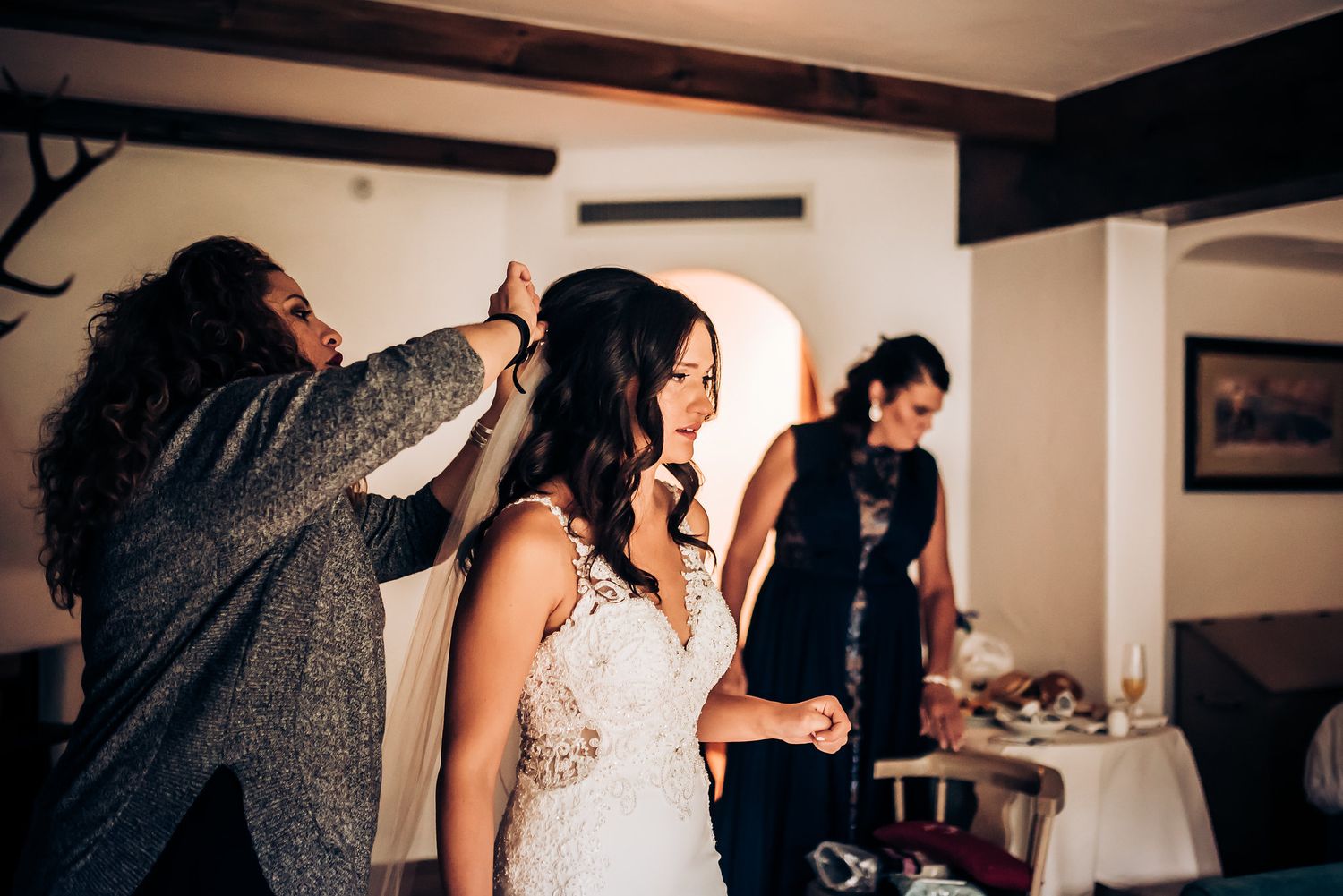A wedding dress being adjusted during final preparations in a warmly lit room.
