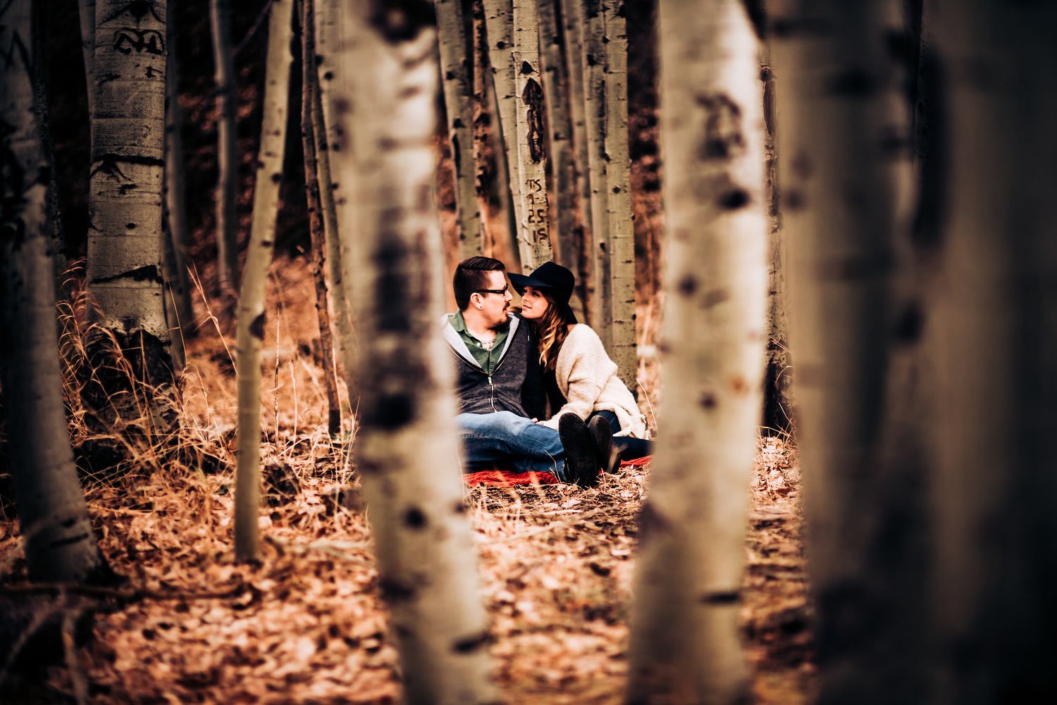 Couple sitting between birch trees in autumn forest during romantic photoshoot.