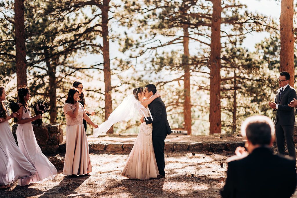 An intimate wedding ceremony unfolds in a serene forest setting with golden sunlight streaming through pine trees.