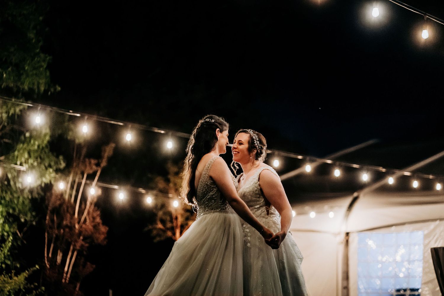 Couple dancing romantically under string lights at evening reception.