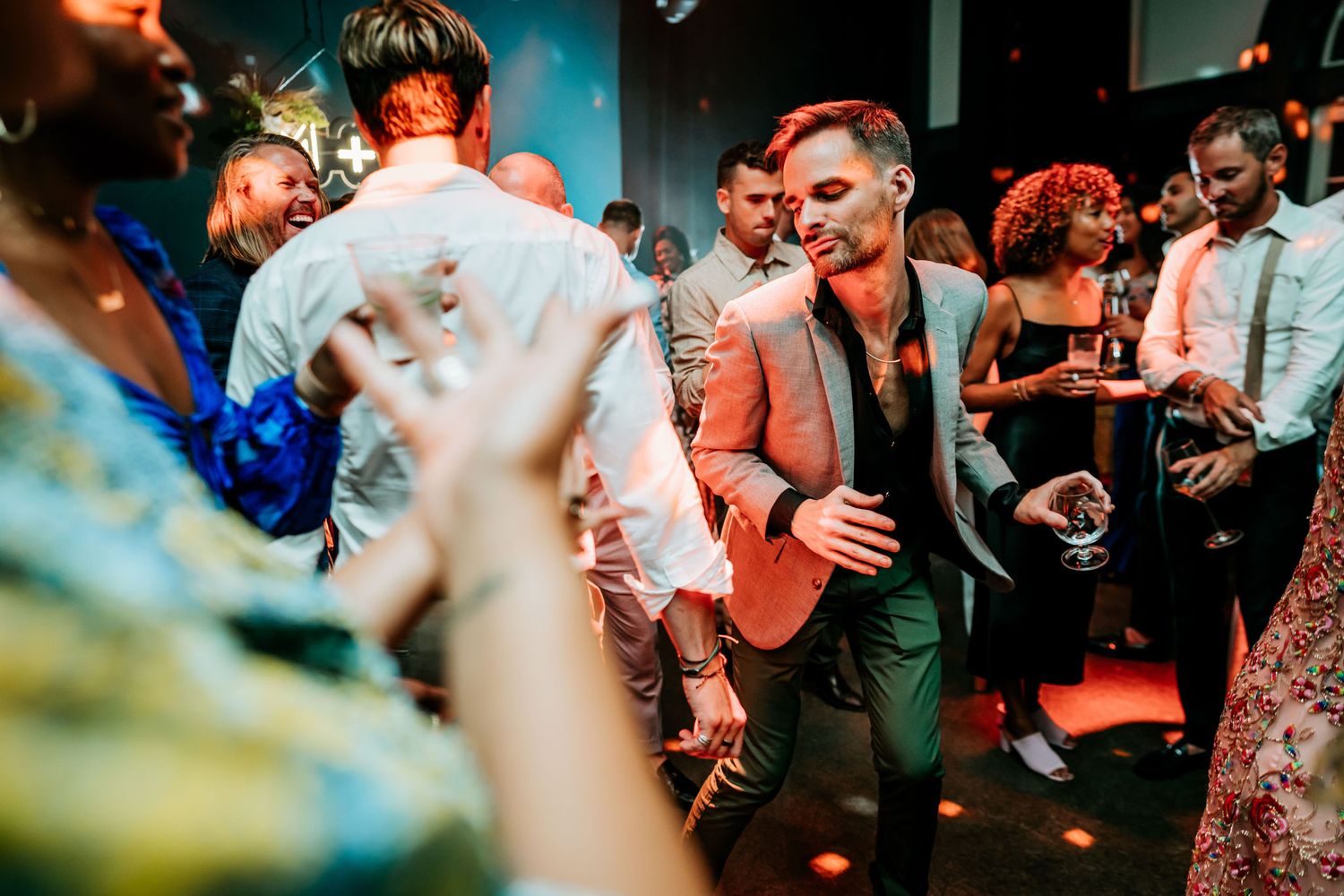 Wedding guests dance energetically on a colorful dance floor as colorful lights illuminate the celebration.