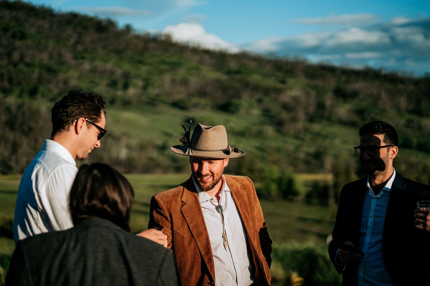 Group gathered outdoors against backdrop of green rolling hills under blue sky.