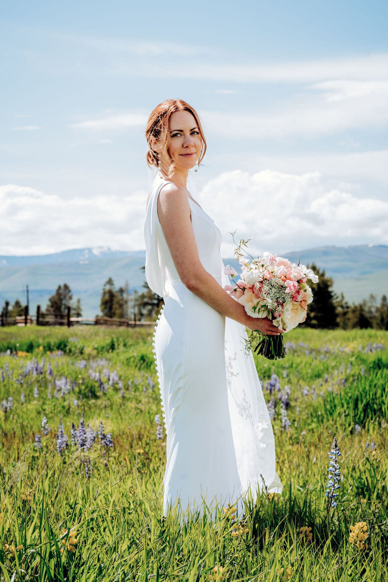 Bride holds a beautiful pink and white bouquet while standing in a wildflower meadow.