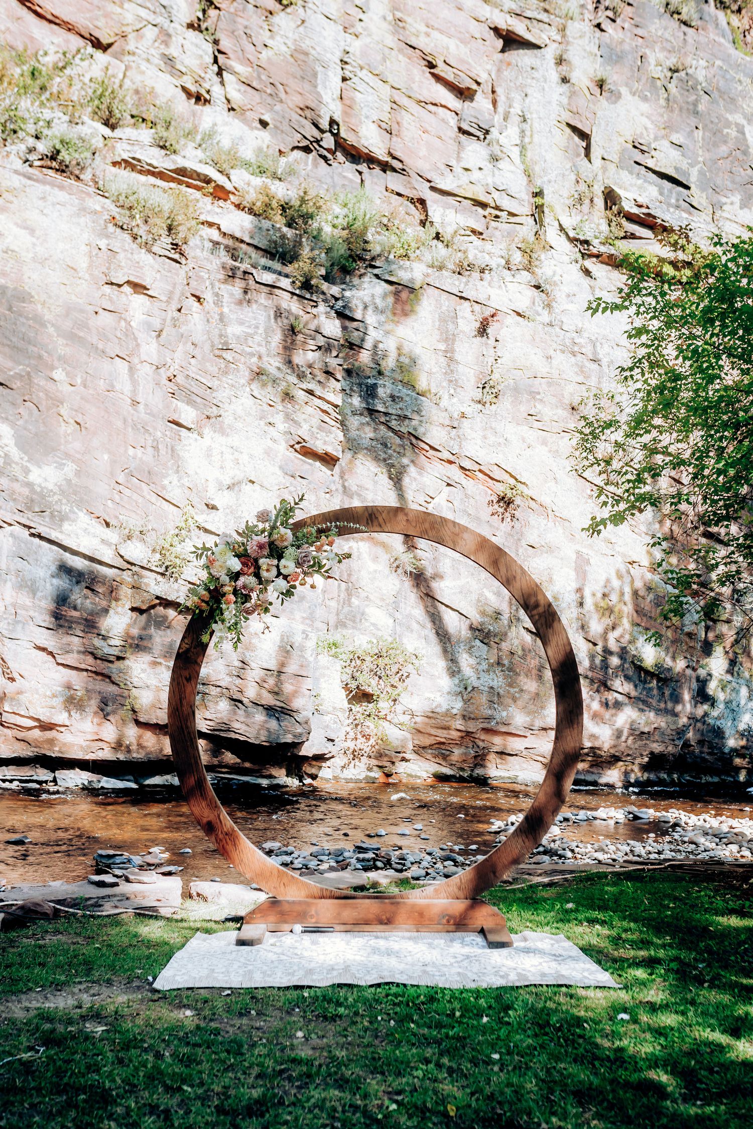 A circular copper wedding arch installation against a dramatic rocky cliff backdrop.