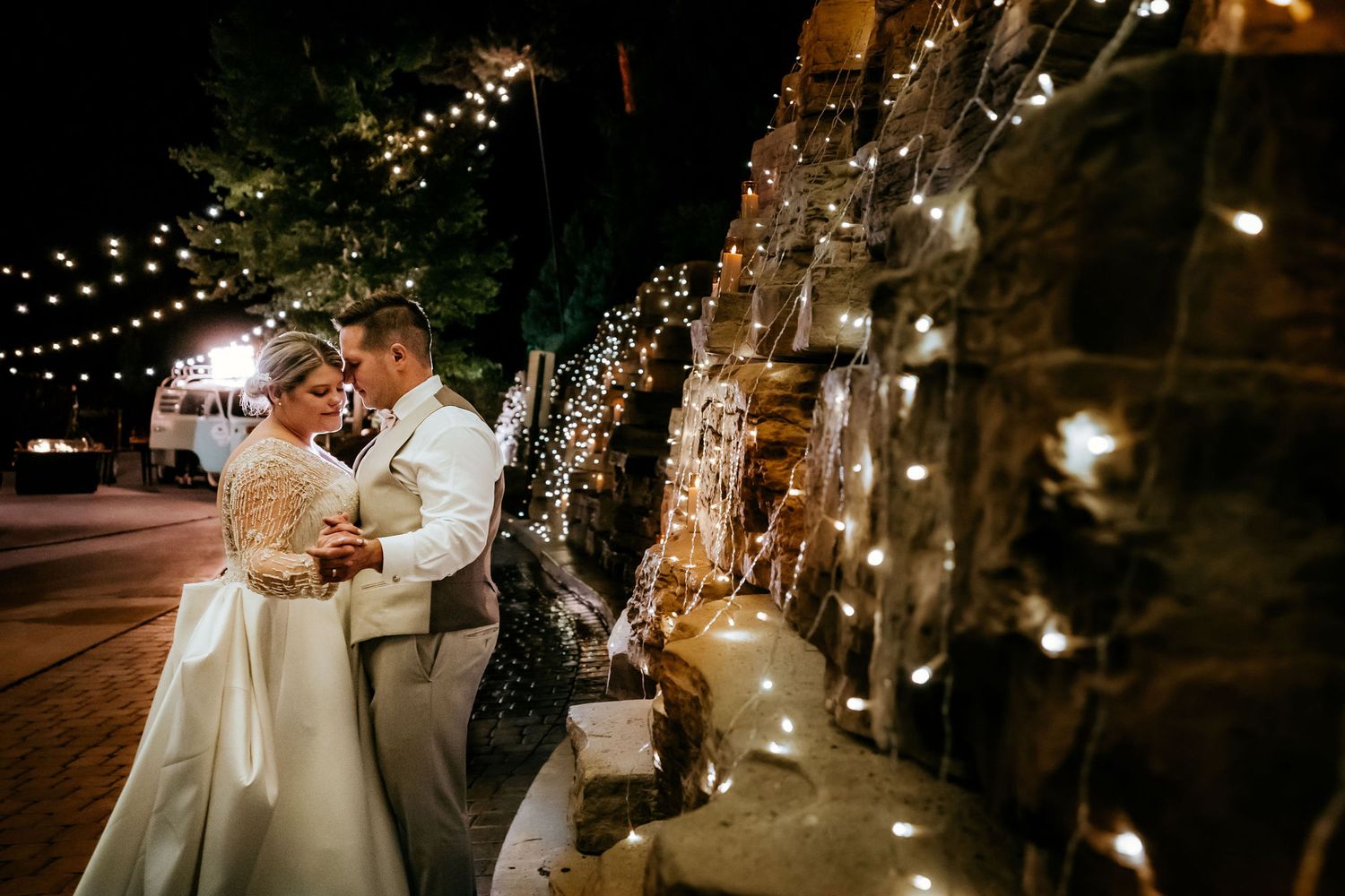 Romantic evening portrait with twinkling lights and stone wall creating magical ambiance.