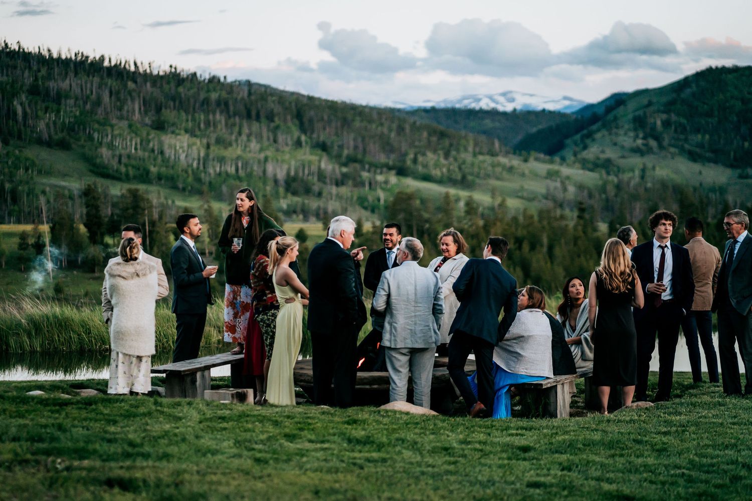 Wedding guests gathered on mountainside overlooking scenic valley landscape.