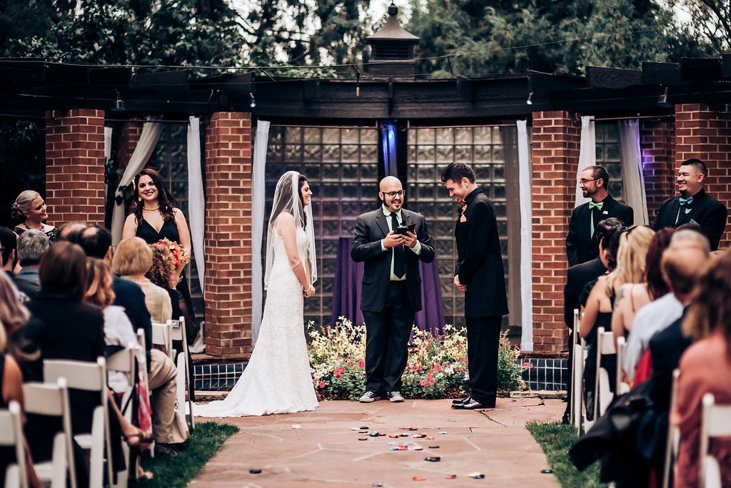 Wedding ceremony in garden setting with brick pergola and white chairs for guests.