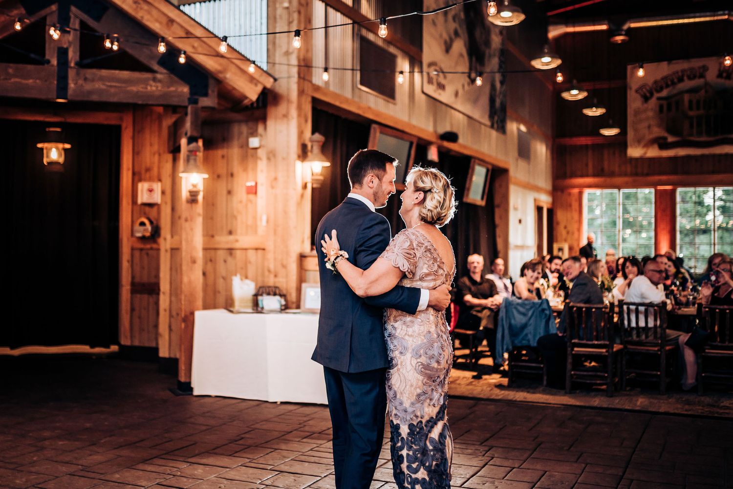 Couple shares their first dance in rustic venue with wooden beams and string lights.