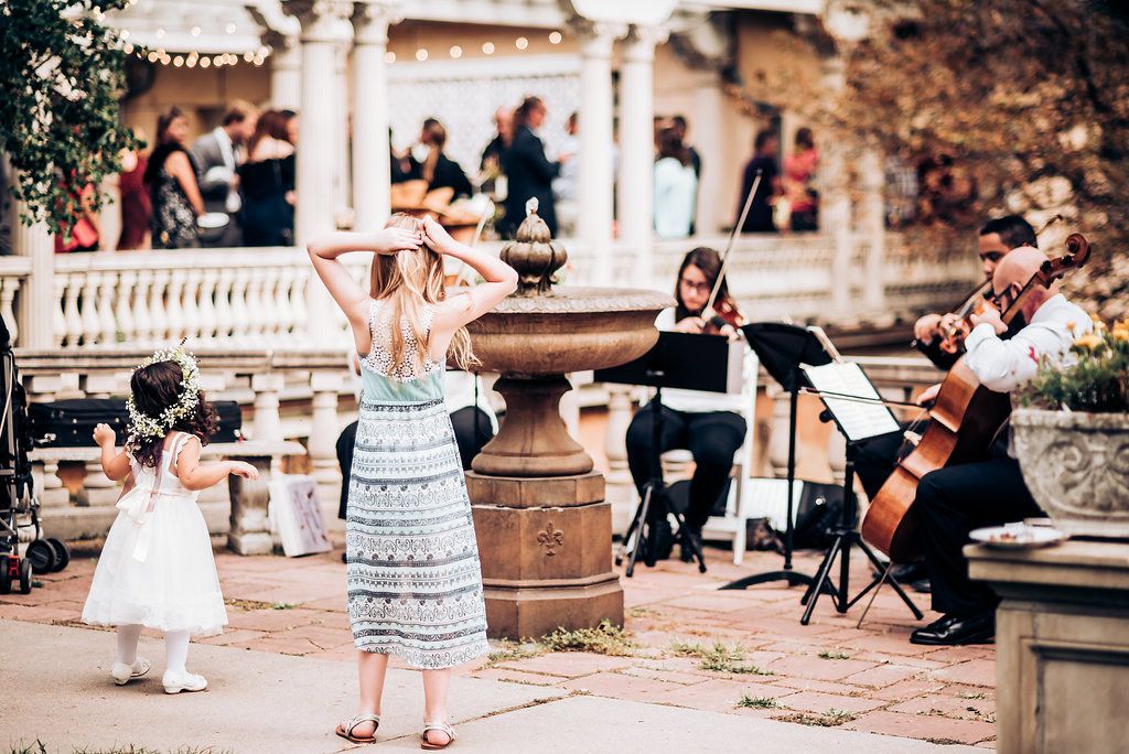 Musicians perform at an outdoor event while a young guest in a light dress dances.