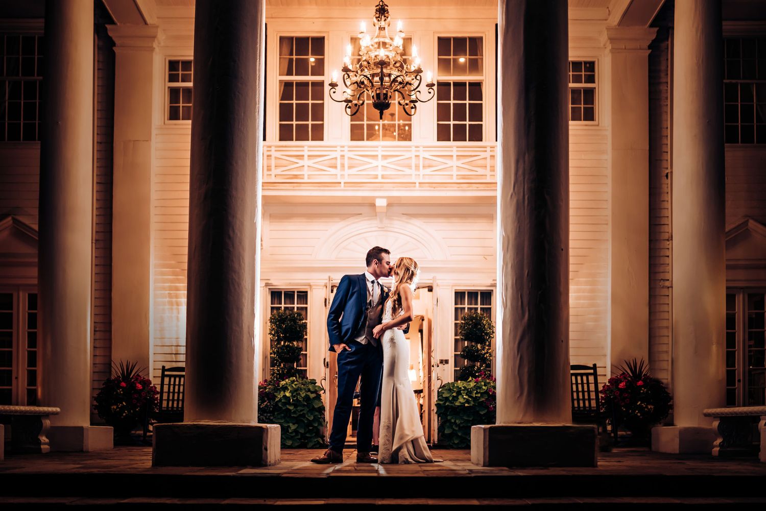 A stunning nighttime wedding portrait on a grand pillared porch with classical architecture.