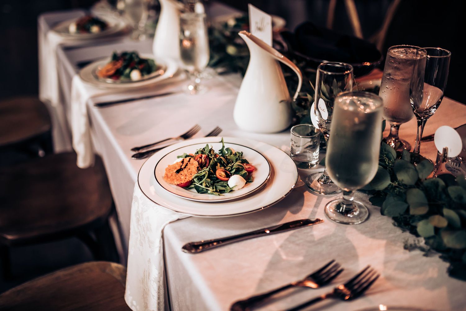 Formal place setting with plated meal, wine glasses and white linens at wedding reception.