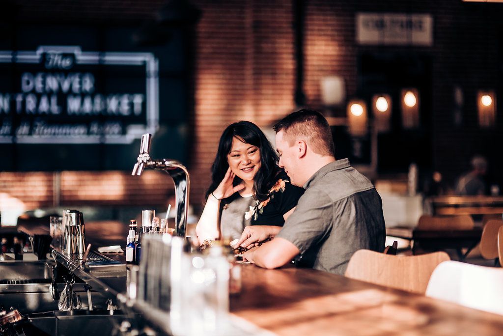 A couple enjoying drinks together at a dimly lit bar counter near Denver Central Market.